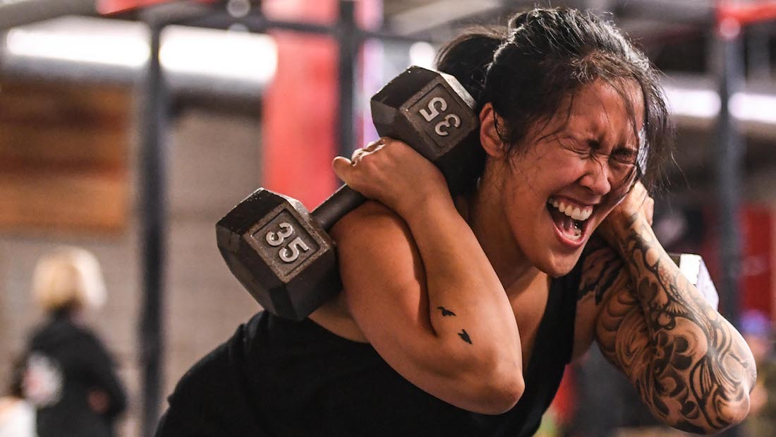 Grimacing woman squats with two 35-lb. dumbbells